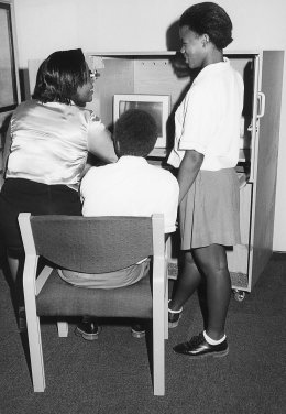 Umkhumbane Library Assistant, Gugu Dladla, explains how information is accessed to two school pupils.